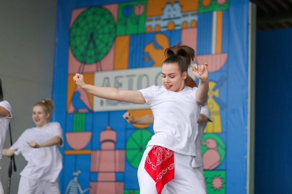 Group of women performing a lively dance on a vibrant stage background.