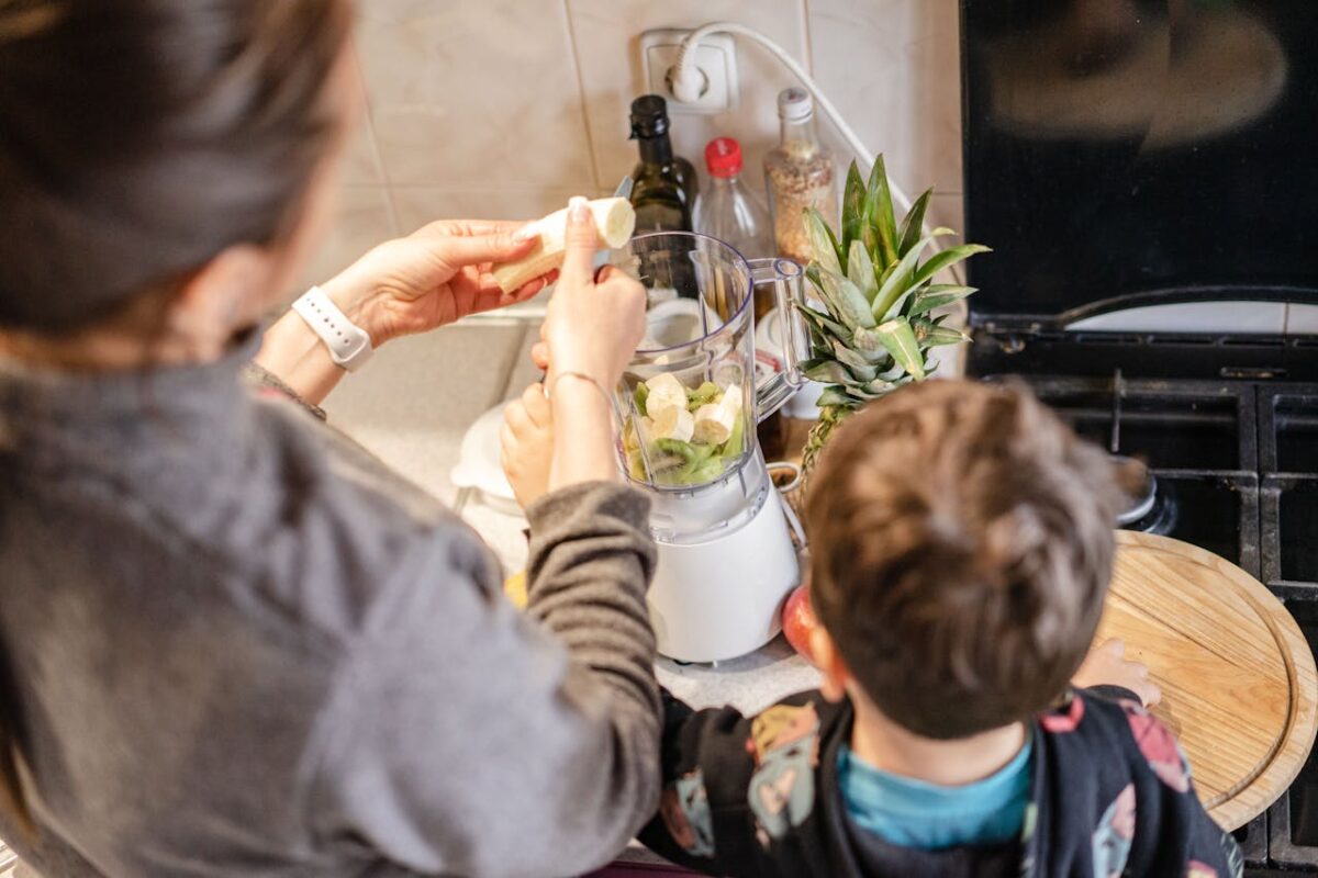 Mother with child making a healthy fruit smoothie in the kitchen, using bananas and pineapples.