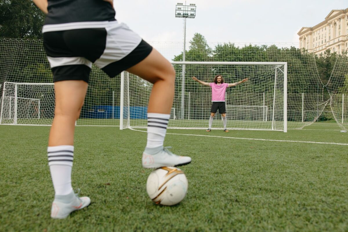 Soccer player in action aiming for the goal with a goalkeeper ready to defend.